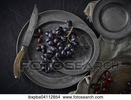 Picture - Pewter plates with grapes on a black underground. Fotosearch
