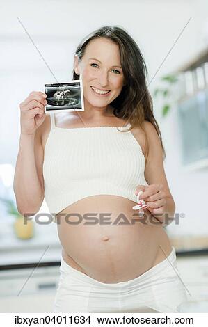 Pregnant woman holding an ultrasound image View Large Photo Image Picture - Pregnant woman holding an ultrasound image. Fotosearch