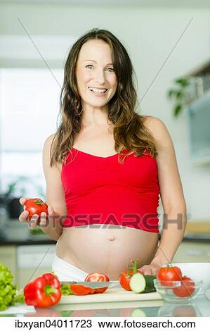 Stock Image - Pregnant woman posing with vegetables. Fotosearch