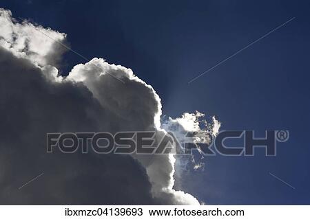 Stock Image - Rain clouds, nimbostratus, against a blue sky with bright sun rim. Fotosearch