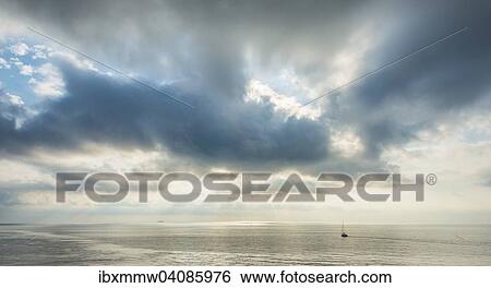 Stock Photograph - Sailing boat in the sea, against dramatic clouds, France, Europe. Fotosearch