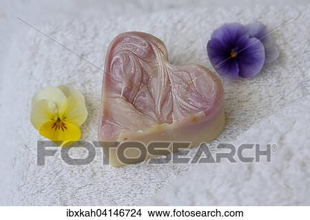 Picture - Soap in heart shape on terry towel with flowers of horned violets. Fotosearch
