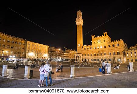 Stock Image - Tourists at the Palazzo Pubblico with illuminated Mangia Tower and chapel, night, Piazza Il Campo, Siena, Tuscany, Italy, Europe. Fotosearch