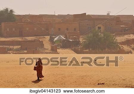 Stock Image - Woman in a dry riverbed, Wadi or Oued, in front of the historic centre, Chinguetti, Adrar Region, Mauritania, Africa. Fotosearch