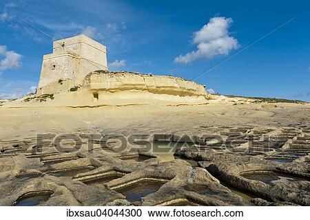 Stock Image - Xlendi Tower, coastal watchtower on a yellow sandstone cliff, sea salt extraction in salt pans, Xlendi, Gozo, Malta, Europe. Fotosearch
