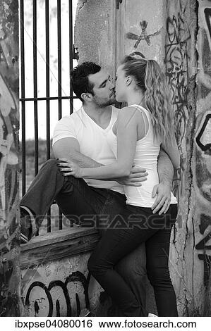 Stock Photograph - Young couple kissing at a barred window in a ruined building covered in graffiti. Fotosearch