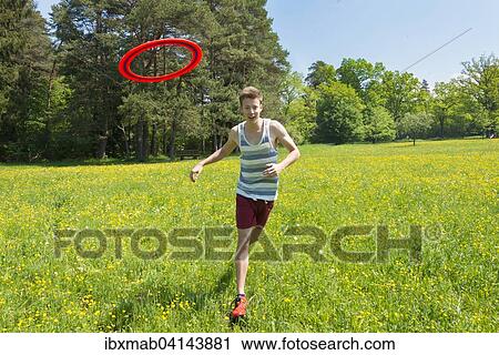 Stock Image - Young man chasing frisbee in meadow, Perlacher Forst, Munich, Bavaria, Germany, Europe. Fotosearch