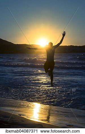 Stock Image - Young man, silhouette, jumping on the beach at sunset, sunset by the sea, Haute-Corse, Corsica, France, Europe. Fotosearch