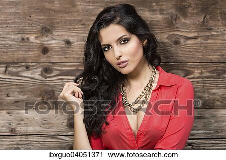 Stock Image - Young woman in a red shirt, in front of wooden wall. Fotosearch