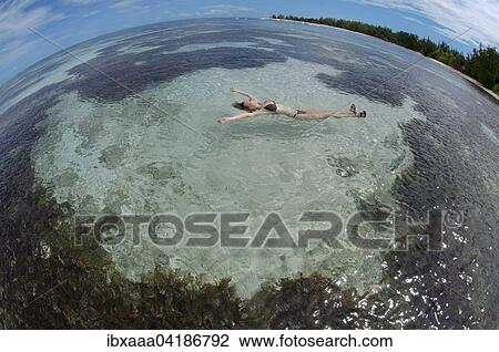 Stock Image - A young woman lying in the water on her back, Denis Island, Seychelles, Africa. Fotosearch