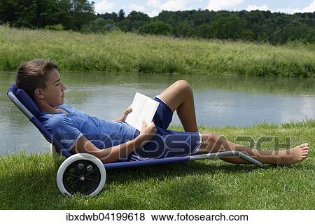 Boy lying in a deck chair, reading a book, next to the river, Loisach, Upper Bavaria, Bavaria, Germany, Europe View Large Photo Image Stock Photo - Boy lying in a deck chair, reading a book, next to the river, Loisach, Upper Bavaria, Bavaria, Germany, Europe. Fotosearch