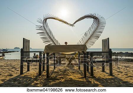 Stock Photograph - Laid table with a heart of palm fronds, sunset, Koh Samui, Gulf of Thailand, Thailand, Asia. Fotosearch