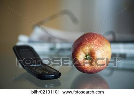 Stock Image - Apple, mobile phone, newspaper and glasses lying on a glass table. Fotosearch