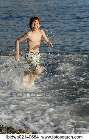 Boy running in the water on a beach by the sea View Large Photo Image Picture - Boy running in the water on a beach by the sea. Fotosearch