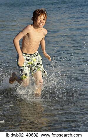 Stock Image - Boy running in the water on a beach by the sea. Fotosearch