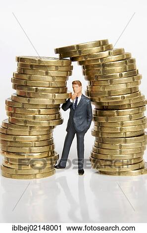 Stock Image - Businessman, figurine, between stacks of coins. Fotosearch