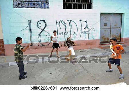 Stock Image - Children playing in front of a wall with graffiti of the criminal Mara 18 gang of youths, Lomas de Santa Faz slum, Guatemala City, Guatemala, Central America, North America. Fotosearch