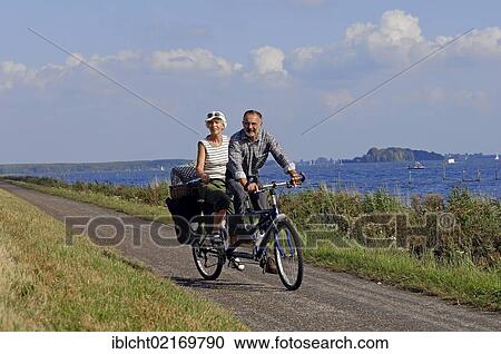 Stock Image - Couple riding a tandem bicycle at Lake Veluwe, Flevoland, The Netherlands, Europe. Fotosearch