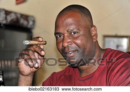 Stock Image - Cuban man smoking a cigar, Santa Clara, Cuba, Greater Antilles, Caribbean, Central America, America, North America. Fotosearch