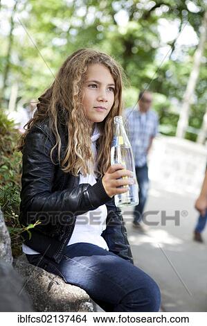 Picture - Girl holding a glass bottle of mineral water and resting. Fotosearch