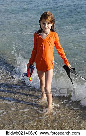 Stock Image - Girl with snorkeling gear, flippers and goggles on a beach by the sea. Fotosearch