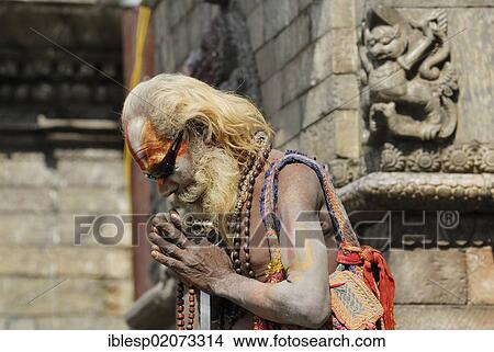 Picture - Holy man, Sadhu, with a painted face, a long beard and sunglasses, Pandra Shivalaya Complex, Pashupatinath on the sacred Bagmati River, Kathmandu, Nepal, Asia. Fotosearch