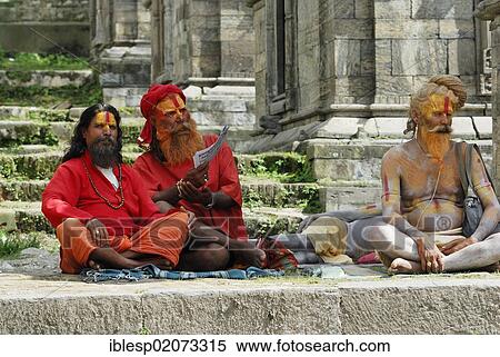 Stock Photography - Holy men, Sadhus, with painted faces, sitting on the steps of the Pandra Shivalaya Complex opposite the ghats of Pashupatinath on the sacred Bagmati River, Kathmandu, Nepal, Asia. Fotosearch