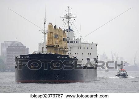 Stock Photo - Large cargo ship is accompanied by a haulier on the Elbe, port, Hamburg, Germany, Europe. Fotosearch