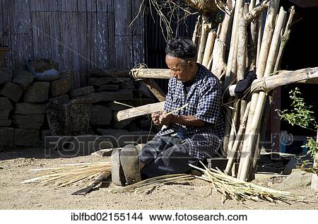 Picture - Man of the Ao tribe braiding in front of his house, Ungma village, Nagaland, India, Asia. Fotosearch