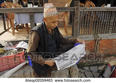 Stock Image - Man with traditional headwear reading the newspaper, Taumadhi square, Bhaktapur, Kathmandu Valley, Nepal, Asia. Fotosearch