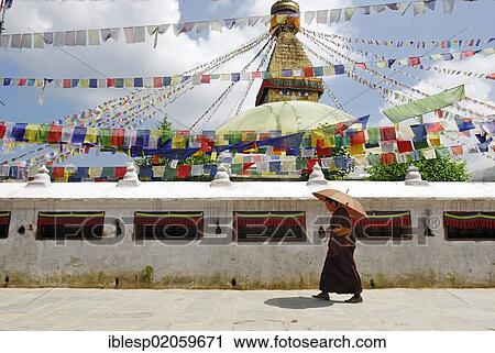 Stock Image - Monk with umbrella, stupa with prayer flags, Boudhanath, Kathmandu, Nepal, Asia. Fotosearch