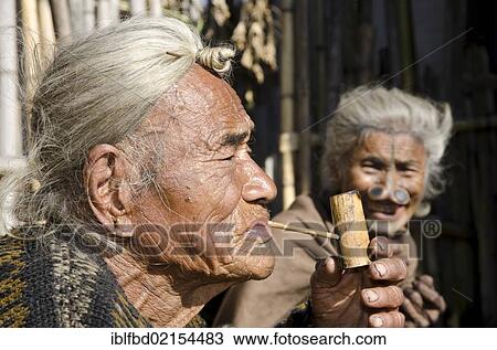 Old Apatani man with the typical hair knot at the forehead, next to a woman with the traditional noseplugs, in front of their house, Hong village, Arunachal Pradesh, India, Asia View Large Photo Image Stock Image - Old Apatani man with the typical hair knot at the forehead, next to a woman with the traditional noseplugs, in front of their house, Hong village, Arunachal Pradesh, India, Asia. Fotosearch