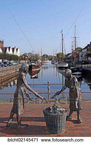 Stock Image - Old Port with the bronze sculpture Toerfwieven, depicting two female peat workers in Weener, East Frisia, Lower Saxony, Germany, Europe. Fotosearch