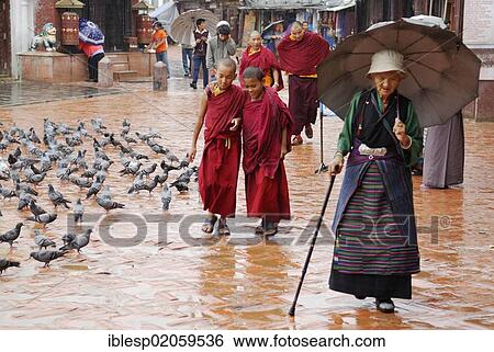 Stock Photograph - Pilgrim carrying an umbrella and monks walking around the Bodnath Stupa in the rain, Kathmandu, Nepal, Asia. Fotosearch