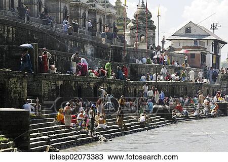 Stock Image - Pilgrims on the steps of the Pandra Shivalaya Complex opposite the Ghats of Pashupatinath on the holy Bagmati River, Kathmandu, Nepal, Asia. Fotosearch