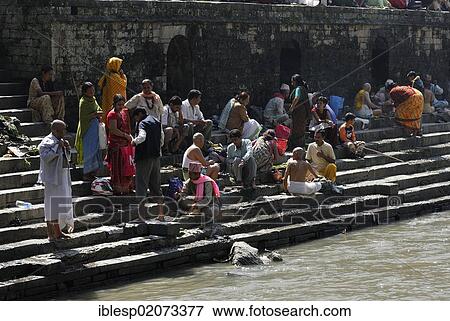 Stock Photo - Pilgrims on the steps of the Pandra Shivalaya Complex opposite the Ghats of Pashupatinath on the holy Bagmati River, Kathmandu, Nepal, Asia. Fotosearch