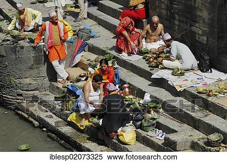 Stock Photography - Pilgrims on the steps of the Pandra Shivalaya Complex opposite the ghats of Pashupatinath on the sacred Bagmati River, Kathmandu, Nepal, Asia. Fotosearch