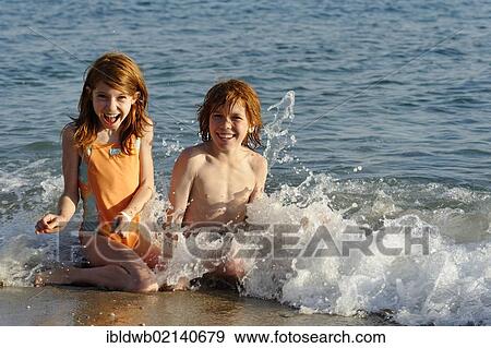 Sister and brother sitting in the water at a beach and having fun in the waves View Large Photo Image Stock Photo - Sister and brother sitting in the water at a beach and having fun in the waves. Fotosearch