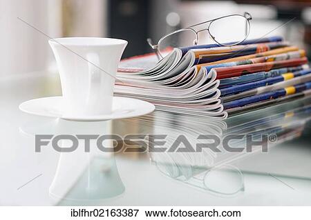 Stock Photo - Still life with magazines, a coffee cup and a pair of glasses on a glass table. Fotosearch