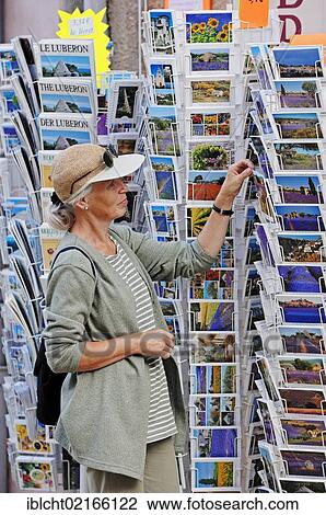 Stock Image - Woman looking at postcards outside a souvenir shop, Sault, Vaucluse, Provence-Alpes-Cote d'Azur, Southern France, France, Europe, PublicGround, Europe. Fotosearch