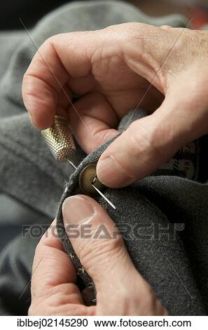 Stock Image - Woman's hands sewing a button on. Fotosearch
