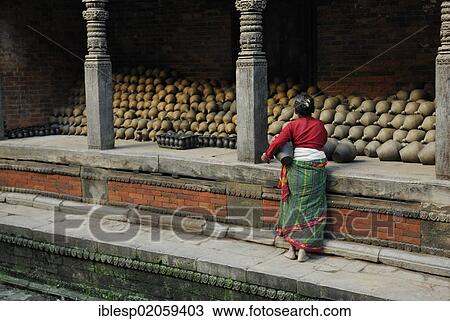 Stock Image - Women in traditional dress standing in front of stacked pottery, Bhaktapur, Kathmandu Valley, Nepal, Asia. Fotosearch