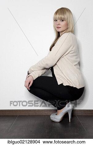 Picture - Young blond woman posing while squatting. Fotosearch