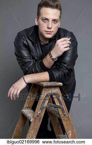 Young man in a leather jacket smoking a cigarette, leaning on a ladder View Large Photo Image Stock Photograph - Young man in a leather jacket smoking a cigarette, leaning on a ladder. Fotosearch