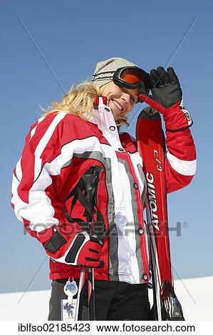 Young woman, about 25 years, wearing a red and white ski suit and a light grey cap, against a blue sky, smiling, one hand on her ski glasses, Thuringian Forest mountains, Thuringia, Germany, Europe View Large Photo Image Stock Image - Young woman, about 25 years, wearing a red and white ski suit and a light grey cap, against a blue sky, smiling, one hand on her ski glasses, Thuringian Forest mountains, Thuringia, Germany, Europe. Fotosearch