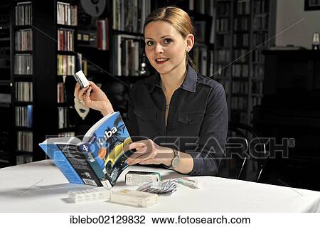 Stock Image - Young woman studying travel guide for an upcoming Cuba trip, checking recommended medication. Fotosearch