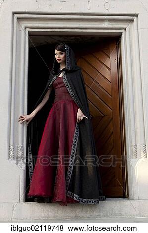 Young woman wearing a red dress and a black cape standing at a door View Large Photo Image Stock Photo - Young woman wearing a red dress and a black cape standing at a door. Fotosearch