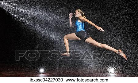 Stock Image - Young woman, 18 years old, jumping in mist, rain. Fotosearch