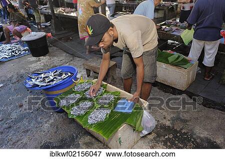Stock Photo - A fish vendor offers tiny fish on a banana leaf for sale at the fish market of the town of Biak, Biak Island, Irian Jaya, Indonesia, Southeast Asia, Asia. Fotosearch