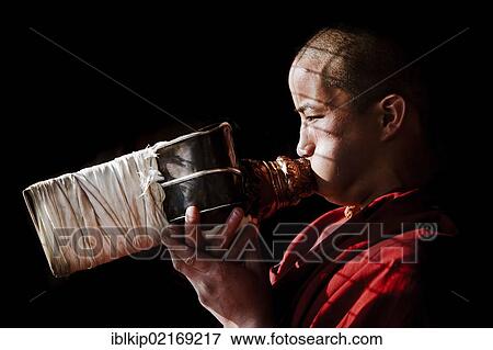 Stock Photo - A young monk facing the rising sun blowing a conch shell trumpet, Tawang Gompa, India, Asia. Fotosearch